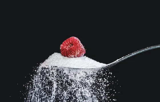 An overflowing spoon of sugar with a raspberry on top